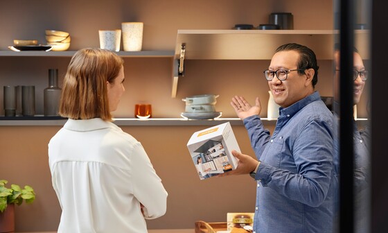 Un expert Blum montre à une femme dans le showroom les possibilités de promouvoir les produits Blum à l’aide de présentoirs.